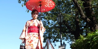 亚洲妇女穿着传统的日本和服，拿着红色的纸伞