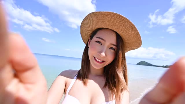 亚洲女人在比基尼拿着相机自画像在白色沙滩上