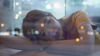 4K孤独年轻美丽的亚洲女人坐在窗前，躺在桌子上，晚上在咖啡馆用智能手机上网。悲伤的少女望着窗外灯火通明的城市街道视频素材模板下载