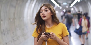 年轻美丽的亚洲女人用智能手机导航走在地铁站里。有魅力的女孩用手机和互联网进行社交媒体或在线信息。无线技术与城市生活理念。