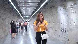 年轻美丽的亚洲女人用智能手机导航走在地铁站里。有魅力的女孩用手机和互联网进行社交媒体或在线信息。无线技术与城市生活理念。视频素材模板下载