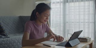 快乐的亚洲女性在家里的客厅里用平板电脑向在线家教挥手或打招呼。提出在家在线学习的概念