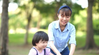 亚洲小女孩学习骑自行车与年轻的母亲在花园视频素材模板下载
