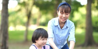 亚洲小女孩学习骑自行车与年轻的母亲在花园