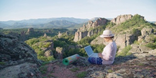 新的标准。新办公室设置。独自旅行的女性，在COVID-19大流行期间，坐在美丽的风景旁边，通过笔记本电脑远程工作。假期和休闲时间。通过社交距离使曲线变平。