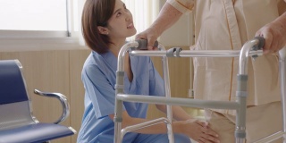 靠近有吸引力的年轻亚洲女人或护士照顾老男人的手杖或步行者感觉有帮助和移情在养老院或医院走廊。老年人的臀部、膝盖和腿部问题。