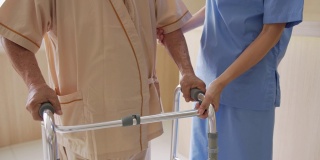 靠近有吸引力的年轻亚洲女人或护士照顾老男人的手杖或步行者感觉有帮助和移情在养老院或医院走廊。老年人的臀部、膝盖和腿部问题。