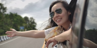 坐在一辆车里的亚洲女人把胳膊伸出车窗，享受，在公路旅行中有乐趣