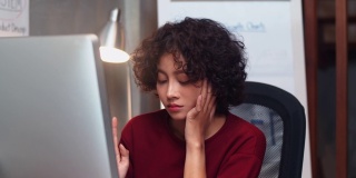 疲惫的年轻亚洲女商人坐在她的办公桌在工作场所。她晚上在办公室工作的时候睡着了。劳累过度的女性感到筋疲力尽，工作让人昏昏欲睡，效率低下。