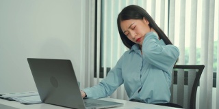 一位年轻的亚洲女性正坐在公司的办公室里，脖子很疼。