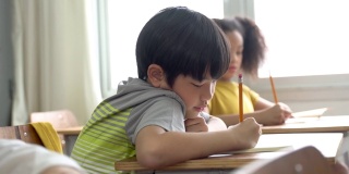 亚洲学校的孩子坐在学校里用铅笔在书上写字，学习，教育，学习。男女学生坐在课桌前写笔记本。小学年龄的男孩和女孩