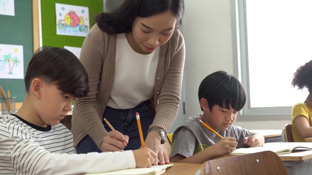 亚洲学校的老师在课堂上帮助学生。年轻女子在学校工作，帮助男孩写作，教育，支持和关心