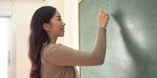 年轻的亚洲女教师在黑板上写数学算术题