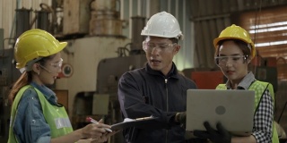 集团工业工程师团队正在工厂洽谈工作。亚洲工头正在向工人介绍建筑工具。操作时戴安全帽。工业机械技术的概念