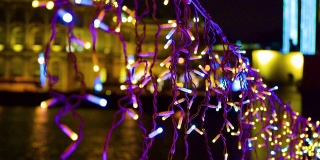节日的装饰彩灯在夜晚悬挂在户外，闪闪发光。模糊的焦散圣诞灯光背景。手持视频