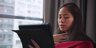 一个多病的年轻女子在用纸巾擤鼻子。坐在沙发上用笔记本电脑