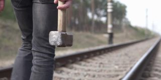 铁路工人手里拿着一把大锤检查铁轨的状况。铁路维护的概念。
