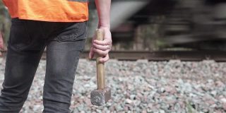 铁路工人拿着一把大锤站在铁路旁边。铁路维护的概念。