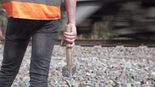 铁路工人拿着一把大锤站在铁路旁边。铁路维护的概念。视频素材模板下载