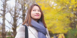 微笑的年轻亚洲女性游客在日本昭和基嫩公园散步，看着美丽的黄色银杏叶在秋天落下的慢动作。日本旅游度假和季节变化的概念。