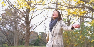 慢动作的微笑亚洲妇女游客享受和有乐趣与投掷黄色银杏叶在秋季在昭和基宁公园在日本。日本旅游度假和季节变化的概念。