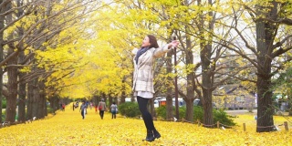 微笑的年轻亚洲妇女游客散步和享受美丽的黄色银杏叶在秋天在昭和Kinen公园在日本。日本旅游度假和季节变化的概念。