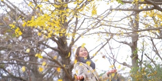 慢动作的微笑亚洲妇女游客享受和有乐趣与投掷黄色银杏叶在秋季在昭和基宁公园在日本。日本旅游度假和季节变化的概念。