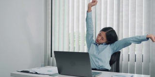 年轻的亚洲女性坐在办公室里舒展肌肉，缓解压力。