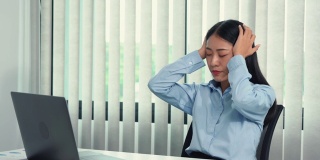 一名亚洲妇女在工作时引起头痛，所以她用手轻轻揉了揉她的头。