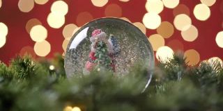 圣诞雪球与圣诞老人和雪花与云杉树枝缓慢旋转的慢动作，以红色背景与散景闪烁的圣诞灯在圣诞夜。