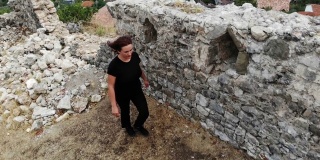 在阿尔巴尼亚，克鲁耶城，女性旅行者在调查古城堡的古老废墟，发现历史，无人机拍摄