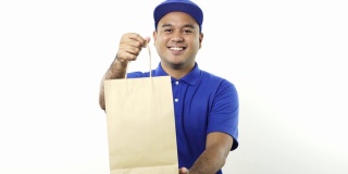 微笑年轻的亚洲快递员在蓝色制服给纸袋的客户在孤立的白色背景。4 k决议。