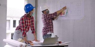 两名建筑工程师戴着口罩，与施工现场的图纸、图纸和布局进行讨论，以保护冠状病毒或新冠病毒和灰尘。建筑工程师的概念。