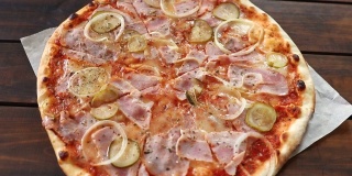 新鲜的圆形披萨，配上马苏里拉奶酪、意大利腊肠、黄瓜和洋葱，在棕色木桌上旋转。披萨店的美味快餐背景