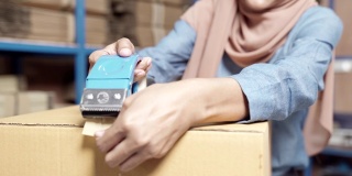 4K超高清近距离手持式:伊斯兰穆斯林女性亚洲仓库工人包装包裹在仓库配送中心。应用于商业仓储物流的概念。