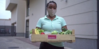 黑人女性志愿者在冠状病毒大流行期间，拿着装着新鲜蔬菜的板条箱，为需要的人运送
