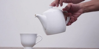 老女人把茶倒进白色背景的杯子里