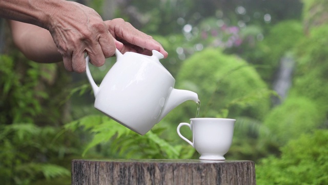 资深女士将香茶倒在以原木和自然为背景的杯子里