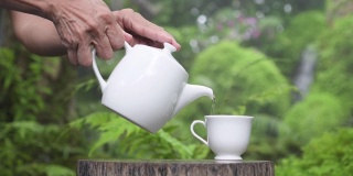 资深女士将香茶倒在以原木和自然为背景的杯子里