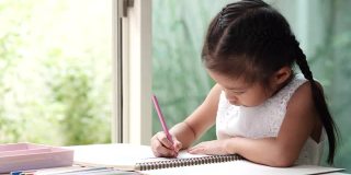 在冠状病毒隔离期间，快乐的亚洲儿童学生或女童使用绘彩铅笔，享受在白纸上写字的乐趣。待在家里，保持社交距离，保护冠状病毒肺炎封锁和学校关闭。