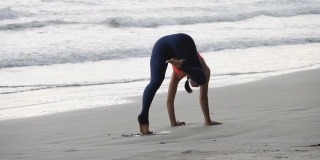 一个亚洲女人正在沙滩上练习瑜伽姿势。经验丰富的女性瑜伽慢动作。健康的生活方式