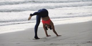 一个亚洲女人正在沙滩上练习瑜伽姿势。经验丰富的女性瑜伽慢动作。健康的生活方式