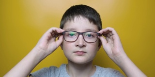 一个可爱的男孩的肖像戴上和摘下眼镜的黄色背景，近视，散光和眼科疾病的概念