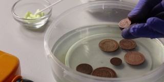 一名男子将铜币放入装有磷酸的容器中，以额外清洗和清除腐蚀残留物。