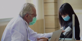 资深医生戴着外科口罩在医院测量血压，用笔记本电脑与年轻的亚洲病人交谈。新冠肺炎大流行或疫情期间的新常态