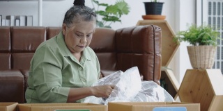 亚洲老年妇女坐在家里分类废物，如玻璃瓶，塑料瓶，金属材料要扔掉。把废物分类再循环再造。保护环境