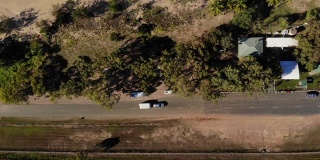 一辆汽车拖着一辆大篷车沿着昆士兰北部的布鲁斯高速公路行驶，沿途是退潮时美丽的海滩。地平线上的岛屿沐浴在金色的阳光下
