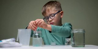 戴眼镜的男孩在室内用吸管和液体做化学实验。学习，有兴趣地学习。选择教育。研究背景。成功学习的个人素质