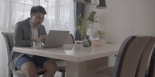 亚洲男人在家工作，在家里餐桌上的临时办公室