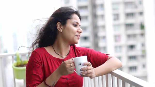 快乐的女人一边喝着咖啡，一边欣赏着阳台上的美景
